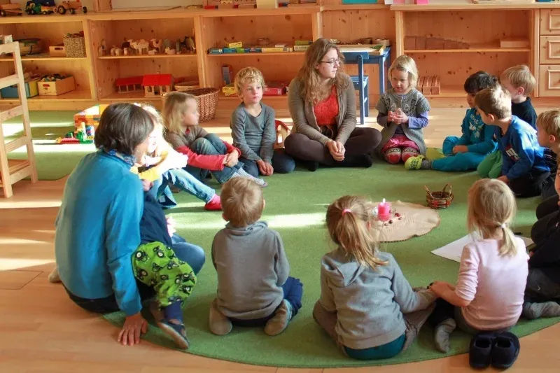 Kindergartenkinder und Pädagoginnen sitzen gemeinsam im Kreis